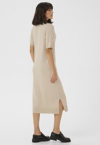 Robe midi en tricot beige à manches courtes, avec fentes latérales et une coupe ajustée. Matériau texturé, finition lisse et design simple.