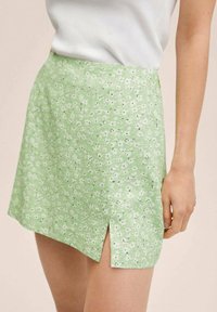 Jupe florale verte avec une texture douce, dotée d'une fente sur le côté et d'un motif de petites fleurs blanches sur un fond vert clair.