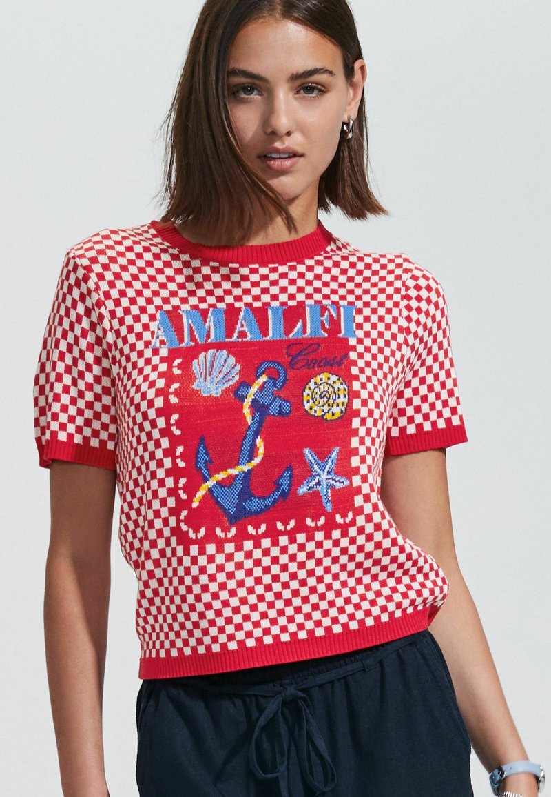 Suéter de punto de manga corta a cuadros rojos y blancos que presenta un diseño bordado de "Amalfi" con conchas y un gráfico de ancla.