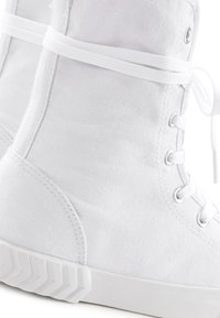 Zapatillas altas blancas de lona, con un acabado texturizado, cordones planos, ojales de metal y una suela de goma con un patrón en zigzag.