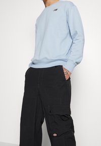 Světle modrá mikina s ribbovanými manžetami a malým logem New Balance; kombinováno s černými cargo kalhotami s kapsami a texturovanou tkaninou.