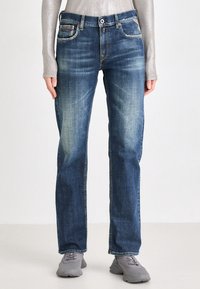 Jeans de mezclilla azul para hombre con un acabado desteñido, corte recto, bolsillos frontales con acentos de costura y cierre de botón.