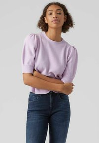 Lys lilla kortermet strikkegenser med puffede skuldre, rund hals og myk tekstur, kombinert med mørk denim jeans.