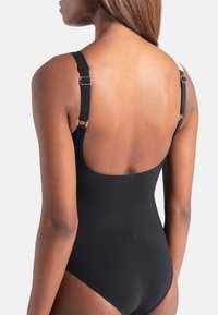 Μαύρο ολόσωμο μαγιό με ρυθμιζόμενους ιμάντες, λεία υφή και σχέδιο με ψηλή πλάτη. Διαθέτει ασημένιες μεταλλικές λεπτομέρειες στους ρυθμιστές των ιμάντων.