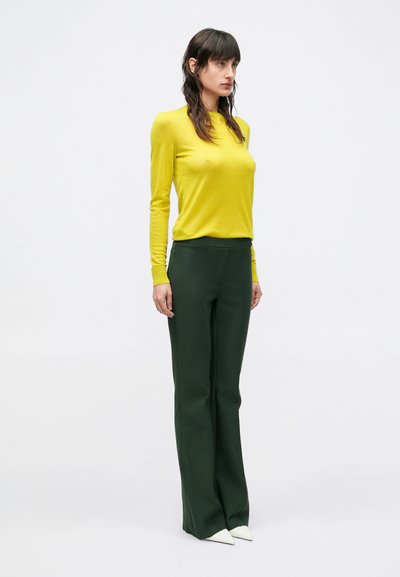 Geel, gebreid top met lange mouwen gecombineerd met nauwsluitende groene broek. De outfit heeft een eenvoudig ontwerp, met een gladde textuur en zonder zichtbare patronen.