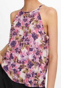 Top sin mangas floral en una tela ligera y transparente. Presenta tonos púrpuras, rosas y verdes con un ajuste relajado y diseño de cuello halter.