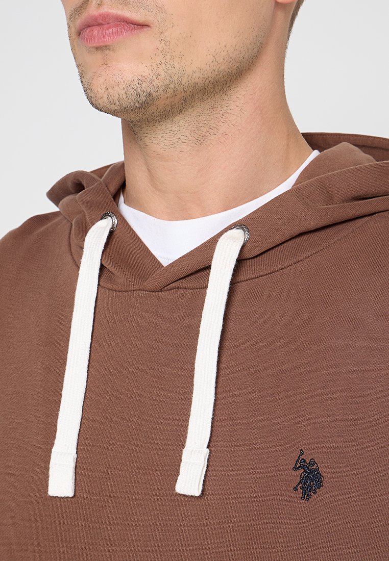 Sudadera marrón hecha de una mezcla de algodón con cordones blancos, bolsillo tipo canguro y pequeño logo bordado en el pecho. Textura suave.