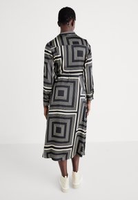 Abito lungo a maniche lunghe bianco e nero con motivi geometrici a quadri, stretto in vita, di lunghezza media e con una texture liscia. Inclusi calzature casual.