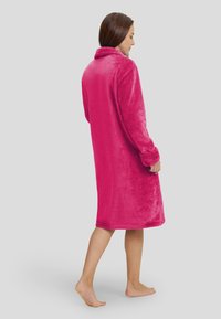 Bata de baño de forro polar en un vibrante color rosa, de longitud hasta la rodilla, con cuello y mangas largas. Textura suave, diseño simple, sin patrones o acentos visibles.