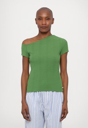 Top verde a costine con scollatura asimmetrica e maniche corte, abbinato a pantaloni a righe blu e bianche.