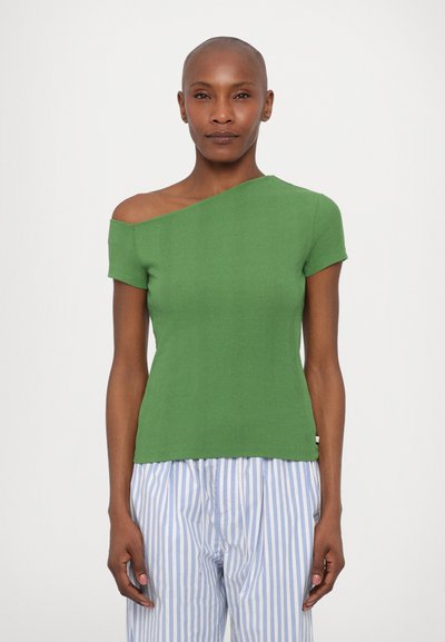 Groene geribbelde trui met een asymmetrische halslijn en korte mouwen, gecombineerd met blauw-wit gestreepte broeken.