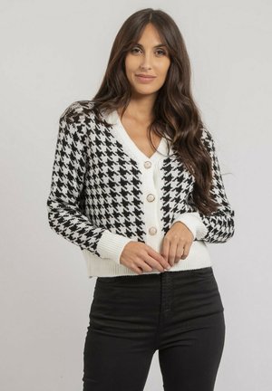 Cardigan en damier noir et blanc avec un col en V, bouton sur le devant, et des poignets et un ourlet côtelés ; fabriqué en matériau tricoté doux.