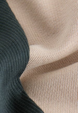 Tessuto a maglia che mette in mostra due colori: verde scuro e beige. Le trame sono a coste e lisce con cuciture fini visibili in tutto.