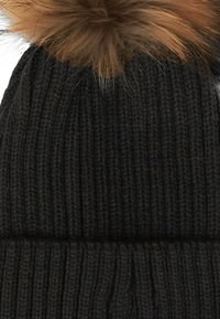 Cappello beanie a coste nere con un grande pompon in pelliccia sintetica marrone sulla cima.