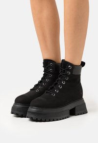 Zwarte veterschoenen tot de enkel, gemaakt van suède en rubber, met een chunky platformzool, metalen oogjes en een gevoerde kraag.