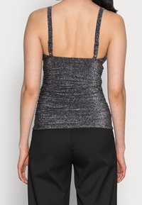 Débardeur en argent métallique avec une texture froncée, des bretelles fines et une coupe ajustée, associé à un pantalon noir à jambes larges.