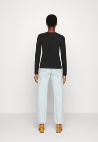 Top preto de manga longa combinado com jeans de perna larga azul claro e sapatos de salto bloco castanhos, visto de costas contra um fundo branco.