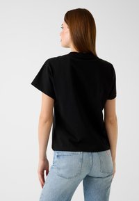 Maglietta nera in cotone con maniche corte, scollo rotondo e una forma comoda, abbinata a jeans di denim azzurro chiaro con tasche posteriori.