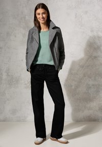 Szary wełniany żakiet, jasna zielona sweter, czarne spodnie o szerokich nogawkach i białe trampki. Żakiet ma kołnierz i detal w postaci zamka.