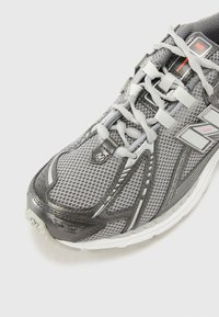 Gray running shoe with mesh upper, reflective accents, and textured overlays. Features gray laces and cushioned sole for support.