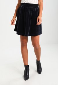 Marinblå sammetkjol med elastisk midja, utsvängd design och mjuk textur, kombinerad med svarta ankelskinnstövlar.