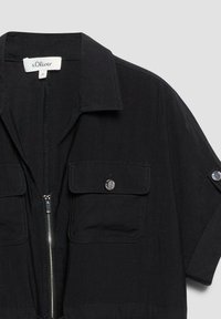 Chemise noire à manches courtes avec fermeture éclair argentée, deux poches poitrine à rabat avec bouton, et col, taille 36 de la marque s.Oliver.