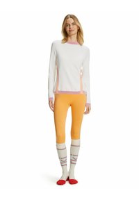 Maglione bianco con accenti rosa e arancione, abbinato a leggings arancioni e calze fino al ginocchio a strisce colorate con suole rosse.