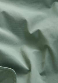 Tissu froissé et mat de couleur verte douce et atténuée avec une texture subtile. Comprend une couture et des bords arrondis.