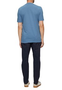 Męska niebieska koszulka z krótkim rękawem, okrągły dekolt, wykonana z miękkiego materiału, zestawiona z ciemnoniebieskimi spodniami i casualowymi butami, widok od tyłu.