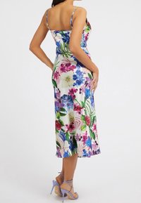 Abito midi floreale con spalline sottili, sfondo prevalentemente bianco, stampe vivaci di viola, rosa e verde, superficie liscia e setosa, indossato con tacchi lavanda.
