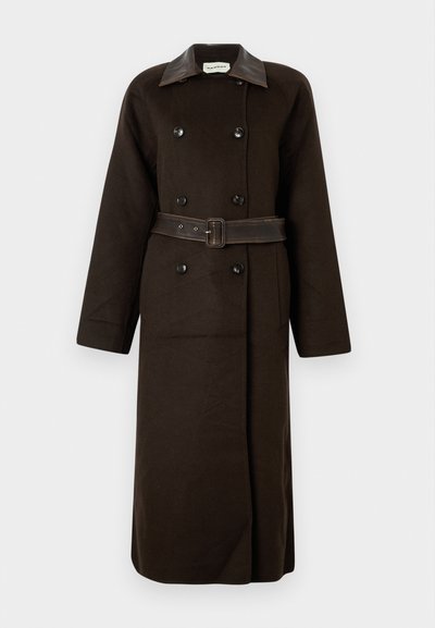 Μακρύ, σκούρο καφέ παλτό διπλής σειράς με μαύρα κουμπιά, φαρδύ δερμάτινο γιακά και αντίστοιχο ζωνάκι που είναι δεμένο στη μέση.