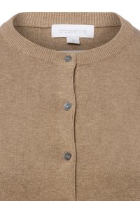 Beige cardigan met een geribbelde halslijn en vijf blauwe knopen. Gemaakt van een zachte gebreide stof. Label met de tekst "brookshire," maat small.