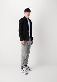 Czarna kurtka z kordurowej tkaniny, szare spodnie cargo i białe sneakersy. Cechy obejmują zapięcie na guziki i jedną kieszeń na klatce piersiowej. Styl casualowy.
