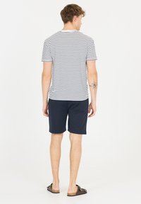 Mans casual outfit med en vit och marinblå randig t-shirt, marinblå shorts och bruna sandaler. T-shirten har en rund halsringning och korta ärmar.