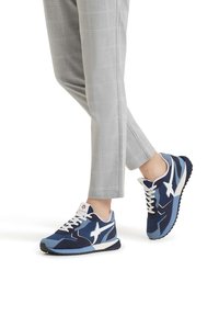 Sneakers blu e navy con accenti bianchi, design con lacci, tessuto testurizzato e suola decorata. Abbinati a pantaloni grigi a quadri.