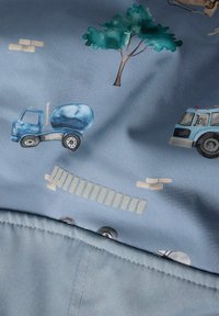 Blauer Stoff mit verspielten Mustern, darunter Baumaschinen, Bäume und Ziegelsteine. Die Oberfläche wirkt glatt mit einem leichten Glanz.