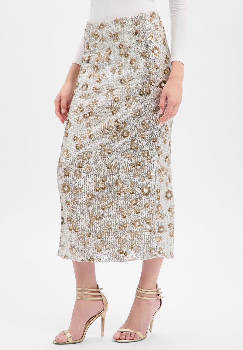 Midi-Rock mit Paillettenverzierung, silberner Grundfarbe mit goldenen Blumenmustern und Fransenstruktur. Kombiniert mit goldenen High Heels mit Riemchen.