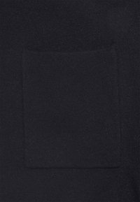 Maglione nero realizzato in materiale morbido con una tasca quadrata sul davanti. La texture appare liscia e leggermente pelosa.