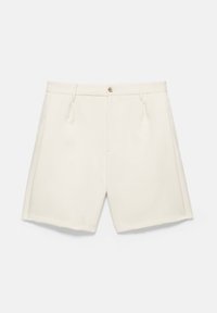 Shorts sur mesure couleur crème, avec passants pour ceinture, poches latérales, bouton à l'avant et braguette zippée, posés à plat sur un fond uni.