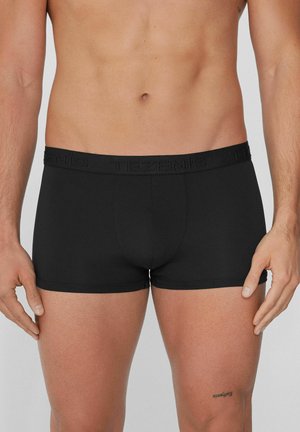 Schwarze Baumwollboxershorts mit einem dehnbaren Bund, der das eingestempelte "TEZENIS"-Logo trägt. Das Design ist figurnah und weist keine zusätzlichen Muster auf.