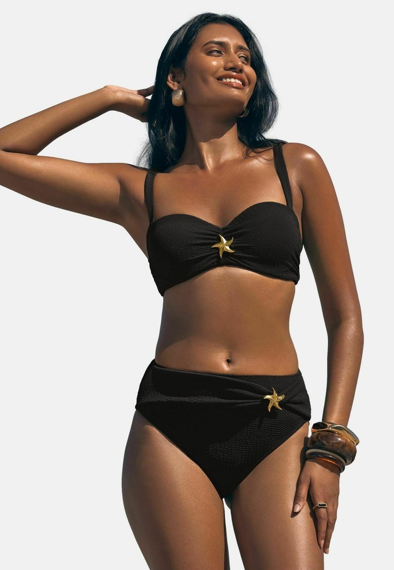 Črni bikini set iz teksturirane tkanine z zvezdo morske zvezde na sredini in hlačkami z visokim pasom. Opremljen z več zapestnicami.