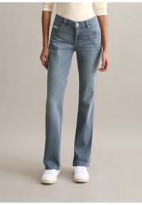 Lichtblauwe spijkerbroek met een rechte pijp, voorzien van voorzakken, een knoopsluiting en subtiele verweerde details. Gecombineerd met witte sneakers.