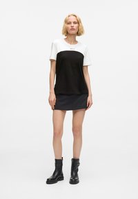 Bluzka t-shirt w kolorze czarno-białym, z okrągłym dekoltem, krótkimi rękawami i luźnym krojem, w zestawie z czarną mini spódnicą i botkami za kostkę.