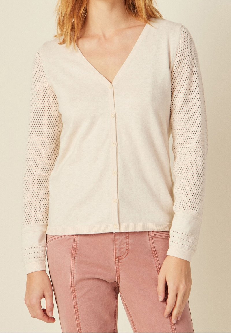 Ljusbeige cardigan med V-hals, knapplist fram och långa stickade ärmar med ett nätmönster. Mjuk textur med ribbade manschetter.