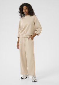Beige sweatshirt with a round neckline and elastic cuffs, paired with wide-leg pants. Both made of smooth fabric. Sports shoes complete the outfit.