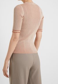 Beige geribbelde gebreide top met korte mouwen, met een textured zigzagafwerking bij de manchetten en een aansluitend ontwerp, gecombineerd met neutrale broeken.