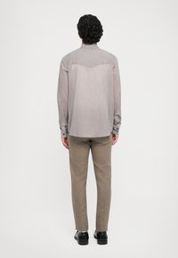 Světle šedá košile s tenkými bílými pruhy, spárovaná s hnědými texturovanými kalhotami. Design obsahuje zádový díl a manžety s ohrnutím.