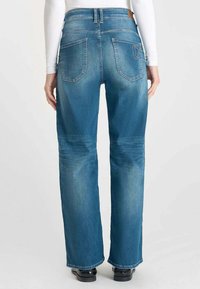 Jeans in denim blu a vita alta e gamba larga. Presentano due tasche posteriori, una leggera scoloritura e cuciture a contrasto. Tessuto morbido con taglio classico.