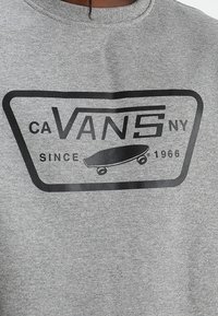 Felpa grigia con logo Vans nero, grafica di uno skateboard e testo "CA Vans NY Dal 1966" sul petto.