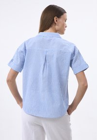 Maglietta a righe con linee blu e bianche, maniche corte, dettaglio con piega sul retro e colletto. Realizzata in tessuto leggero.
